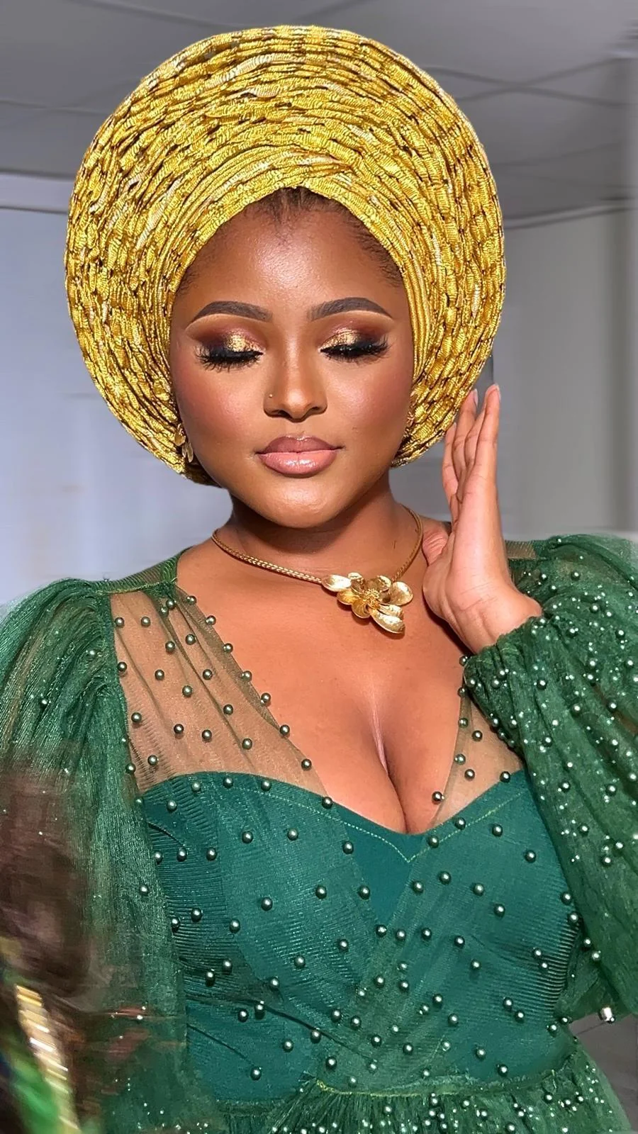 Woman in green wearing a full circular gold gele