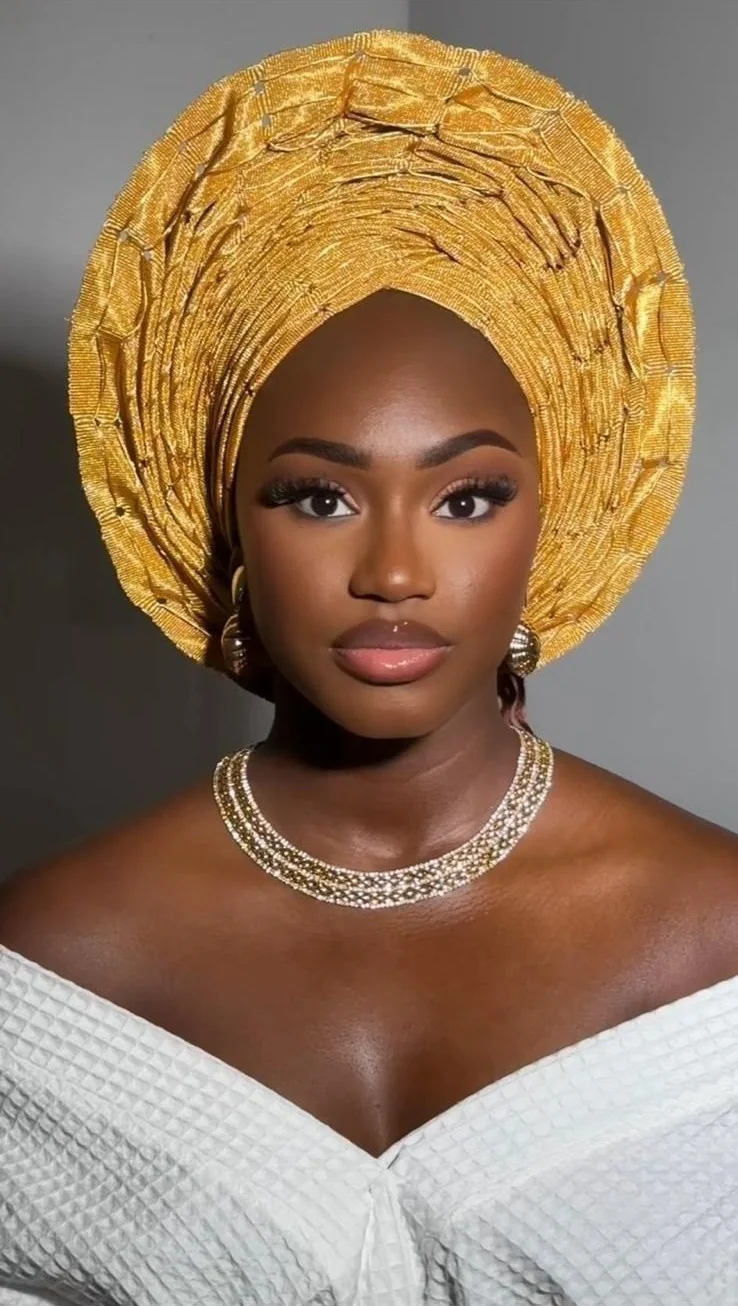 Woman in white wearing a full structured gold gele